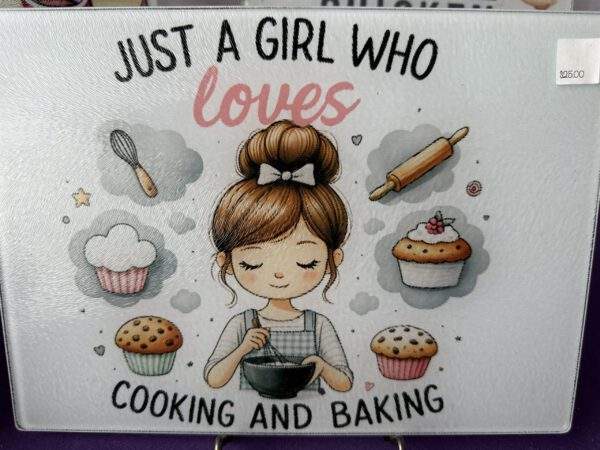 A cute and cozy drawn design on white of a brown-haired girl whisking something inside a bowl while surrounded by cupcakes and baking implements. Text reads, "Just a girl who loves cooking and baking."