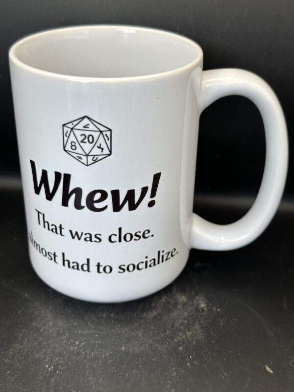 White coffee mug with a D20 dice at the top, above the words, 'Whew! That was close. I almost had to socialize.'