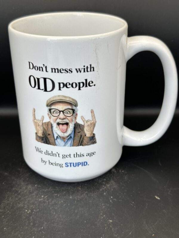 White mug with an elderly man with horn-rimmed glasses sticking out her tongue and making rock and roll 'horns' hands. The text says, 'Don't mess with old people. We didn't get this age by being stupid.'