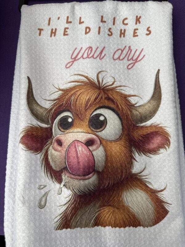 A white dish towel with a cute cow on the front promising, 'I'll lick the dishes you dry'
