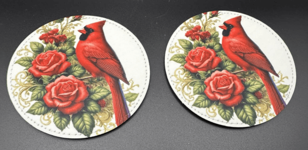 Two white leather coasters are pictured with a red cardinal design on flowers.