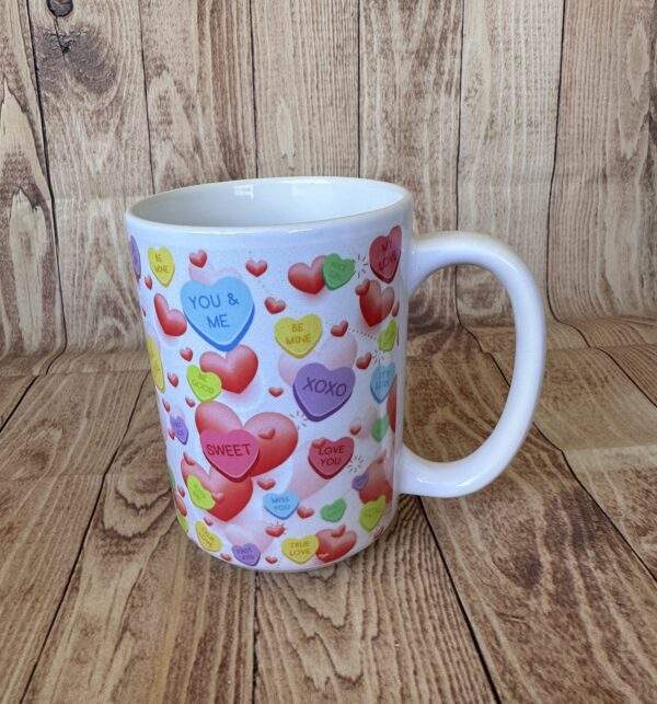 A white mug covered in scatters of candy hearts with Valentine's style messages