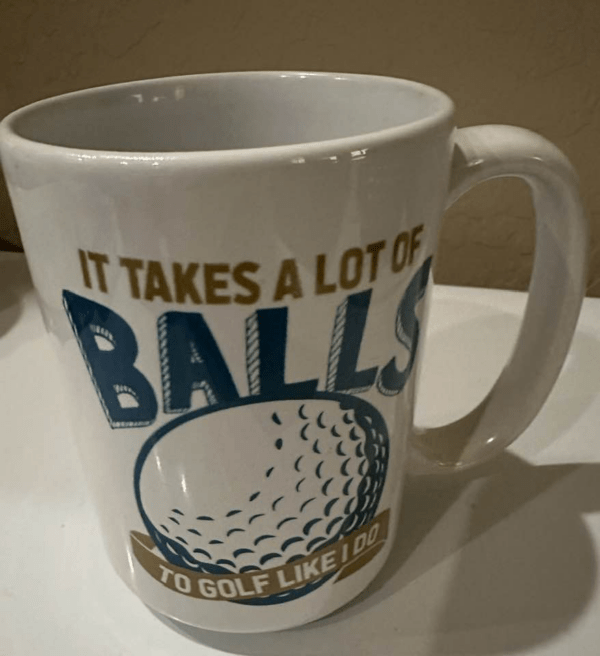 Humorous white coffee mug with an image of a golf ball and the phrase "It takes a lot of balls to golf like I do."