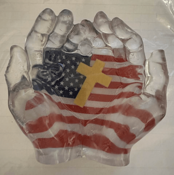 Two large clear resin hands, inside of which is a design of the USA flag and a Christian cross.