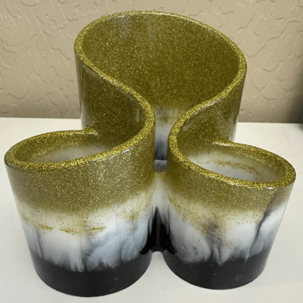 A decorative pen holder with three holding spaces done in resin. Artistically striped in three layers of black, white, and glittering gold.