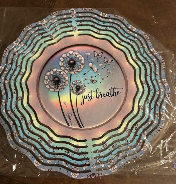 A shiny windspinner and the text 'Just breathe' beside peaceful line-art dandelions and their seeds on the breeze.