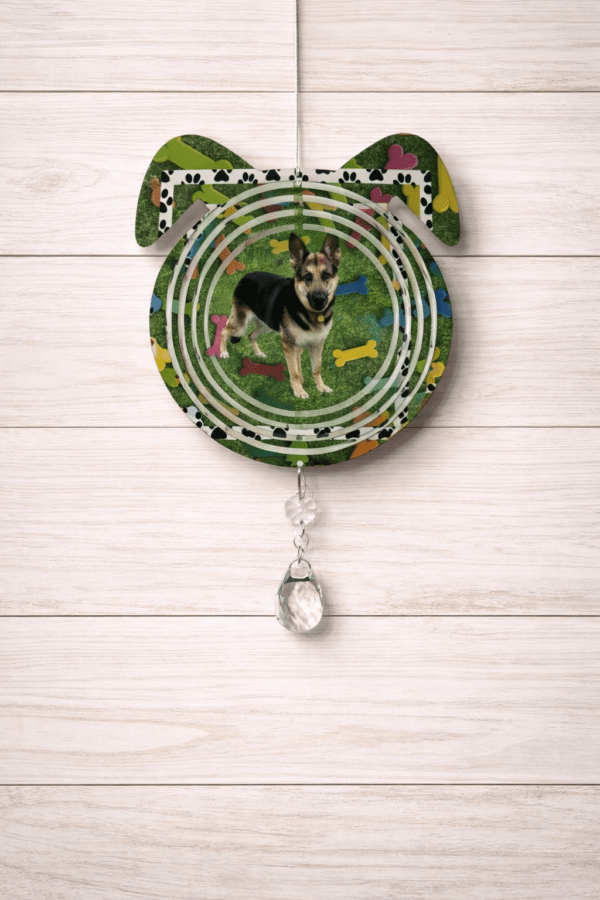 A dog's head shaped windspinner with a design of a German Shepherd on a background of grass and treat bones.