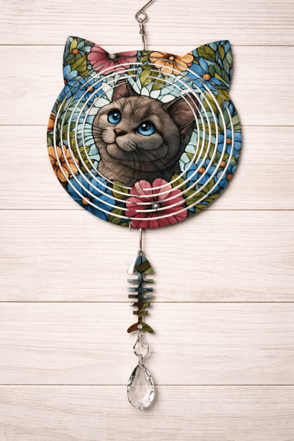 A windspinner with an adorable gray cat with bright blue eyes in a field of flowers. Specialty-cut in the shape of a cat with a fishbone hanging beneath.
