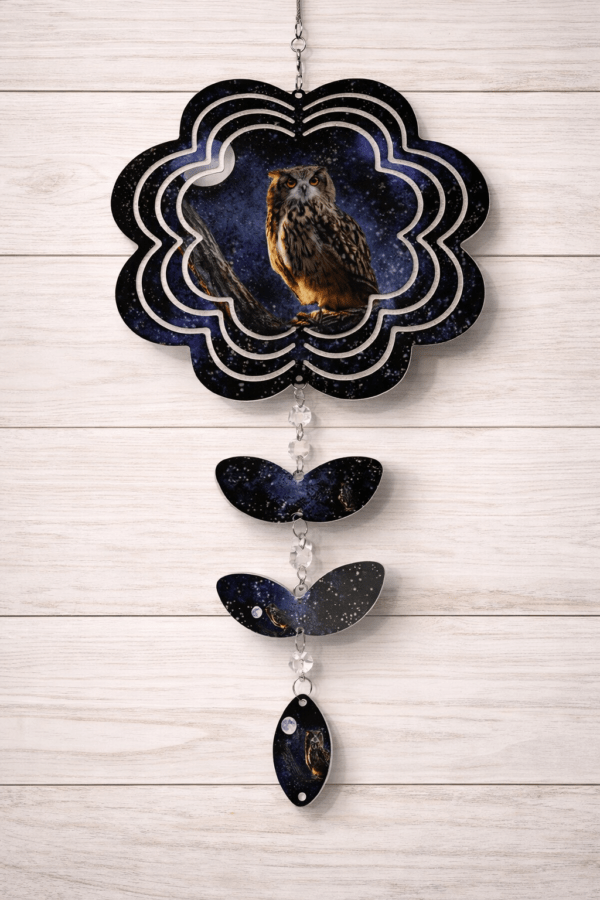 A windspinner cut into the shape of a flower showing the night sky and a peering owl. Leaves and a crystal hang at the bottom.